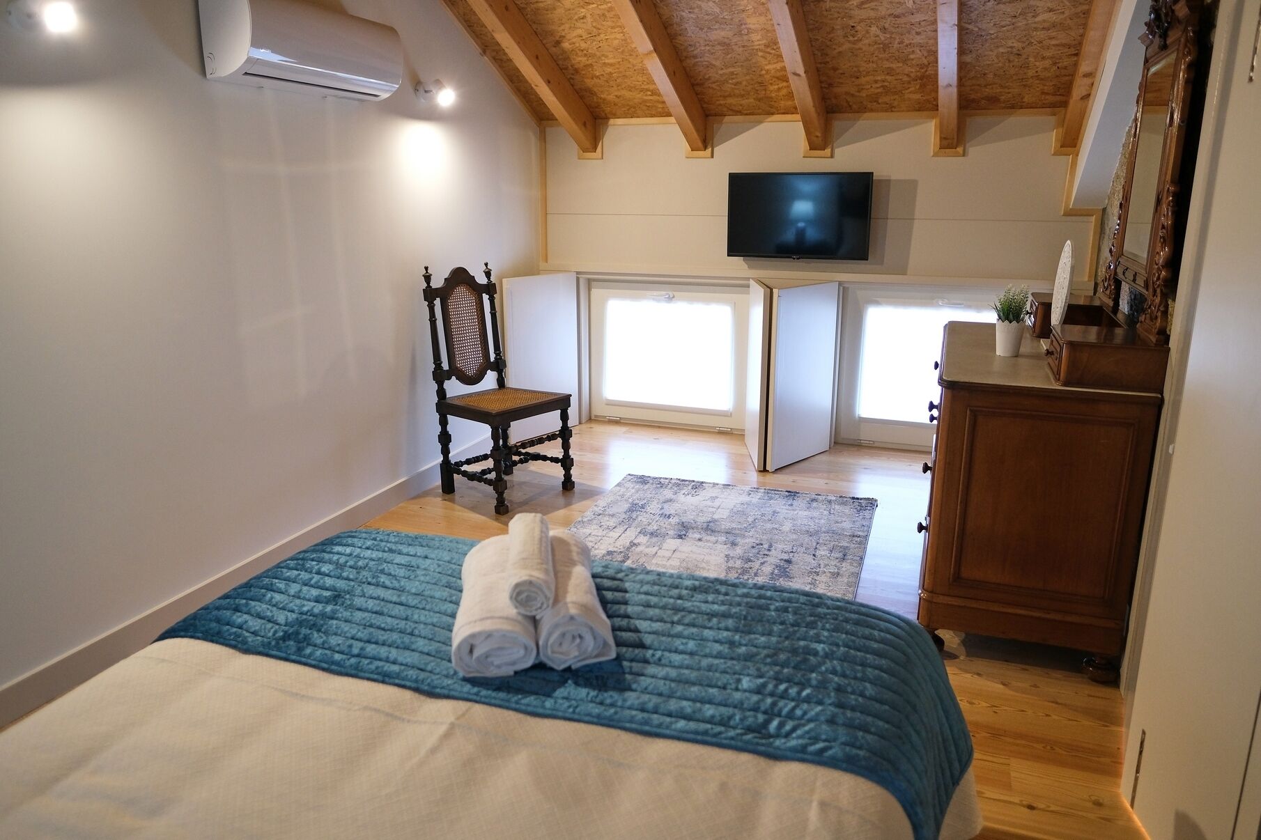 Ein Schlafzimmer mit Bett, Sessel, Fernseher und Kommode.