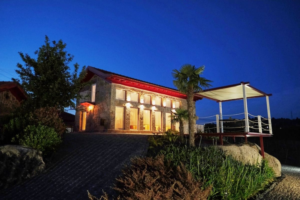 A stone house with a red roof, a covered patio, and a staircase leading to the entrance.