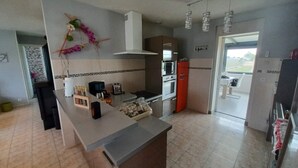 Une cuisine dotée d’un îlot central, d’un four à micro-ondes, d’une cuisinière et d’un réfrigérateur. Une fenêtre laisse entrer la lumière naturelle et offre une vue sur l’extérieur.