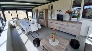 Un salon moderne avec un coin repas, de grandes fenêtres et un téléviseur posé sur un meuble en bois.