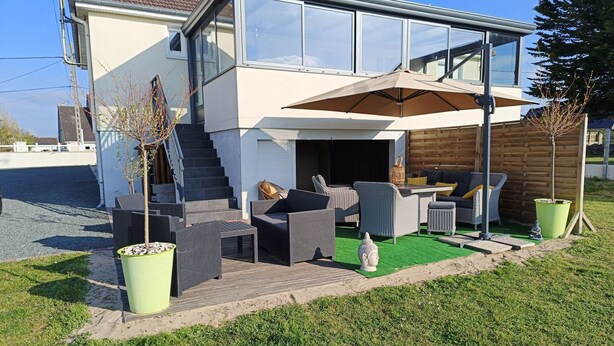 Une maison moderne à deux étages dotée d’un patio aménagé avec du mobilier d’extérieur et un grand parasol.