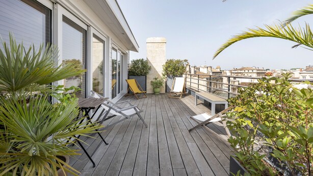 A wooden deck with outdoor furniture, potted plants, and a cityscape view. - Artist Duplex & Terrace - 170m² (Burdeos)