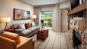 A modern living room with a sofa, armchair, and ottoman, a fireplace, a television, and a large window with a view of greenery. - Large 1-Bdrm Villa in lovely Avon, CO- available wk of July 22-29 (Avon)