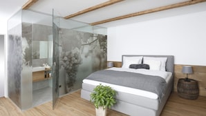 Un dormitorio moderno con cabina de ducha de vidrio, una cama con cabecero gris y suelo de madera.