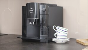 Una máquina de café negra con un panel de control y una pila de tazas a rayas sobre una encimera.