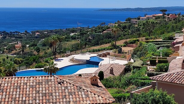 Un resort con piscina, techos de tejas rojas y vista al mar.