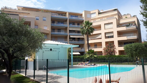 Un edificio residenziale a più piani con balconi, una piscina e una piccola area coperta con indicazioni.