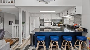 Une cuisine moderne avec des meubles blancs, un plan de travail noir et des tabourets de bar bleus.