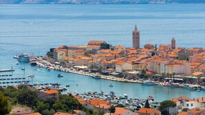 A coastal town with a prominent tower, a marina with boats, and buildings with red-tiled roofs. - Beach front home in Palit with sauna (Palit)