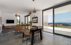 A modern living room with a large TV, comfortable seating, a dining area, and a balcony with a city view. - Beach front home in Palit with sauna (Palit)