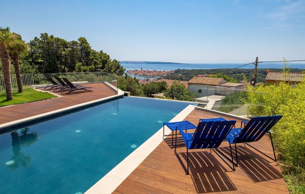 A swimming pool with a wooden deck, blue chairs, and a view of a coastal town. - Beach front home in Palit with sauna (Palit)