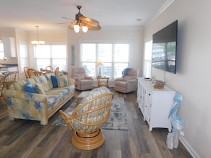 A spacious living room with a sofa, chairs, a dining area, and a TV mounted on the wall.