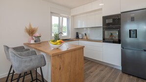 Eine moderne Küche mit weißen Schränken, einem Edelstahl-Kühlschrank, einer Holzinsel mit Obstschale und zwei grauen Barhocker.