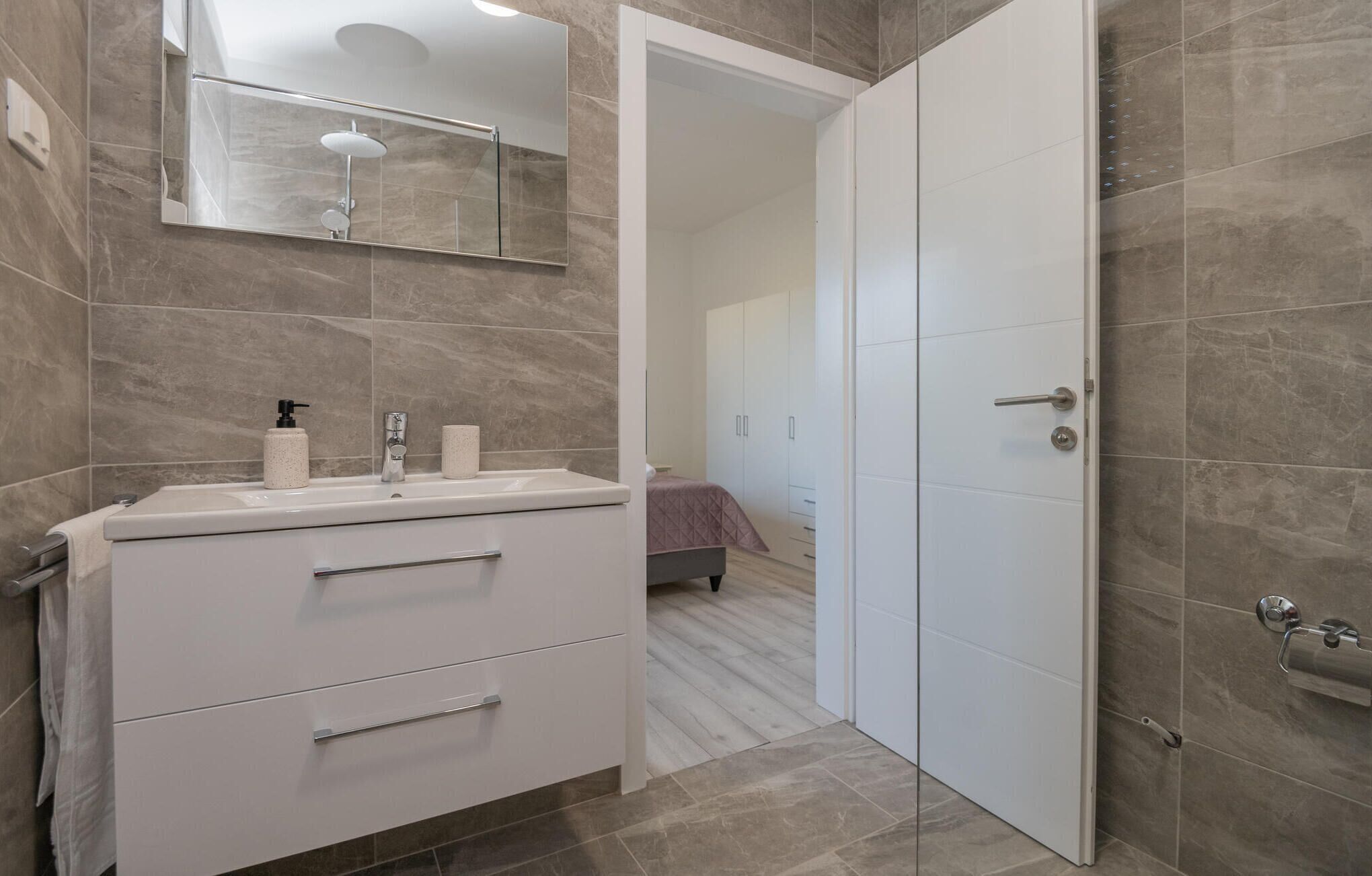A modern bathroom with a white vanity, a large mirror, and a shower area.