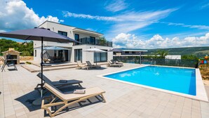 Eine moderne Villa mit Swimmingpool, Sitzgelegenheit im Freien und Kamin aus Stein.
