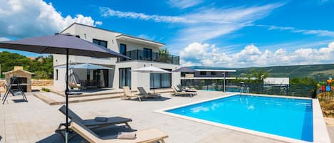 Uma villa moderna com piscina, área de estar ao ar livre e lareira de pedra.