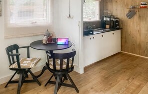 Une petite cuisine équipée d’un évier, de placards et d’une table avec des chaises. Un ordinateur portable est posé sur la table.