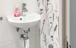 Un lavabo blanc pour la salle de bain, doté d’un robinet moderne, d’un distributeur de savon et d’un rideau de douche orné d’un motif floral.