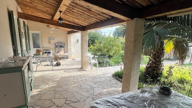 A covered outdoor area with stone flooring, a wooden ceiling, and a view of a garden with a palm tree. - House/Gite/Cottage rated 1 star, with above-ground pool, garden. (Puget-sur-Argens)