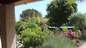 A covered outdoor area with a stone patio, surrounded by various plants and trees. - House/Gite/Cottage rated 1 star, with above-ground pool, garden. (Puget-sur-Argens)