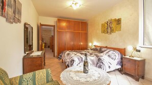 A bedroom with a bed, a bedside table, a chair, a wooden wardrobe, a mirror, and a door leading to another room. - Lovely apartment in Sanremo with WiFi (Sanremo)