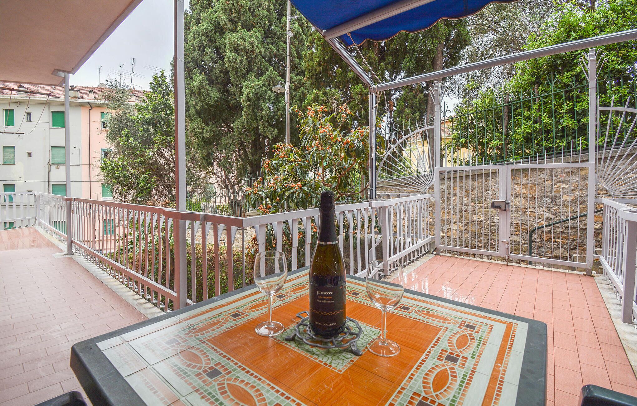 A terrace with a table set for two, a bottle of Prosecco, and a view of the surrounding greenery and buildings.