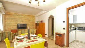 A dining area with a table set for four, a television on the wall, and a kitchen visible through an open doorway. - Lovely apartment in Sanremo with WiFi (Sanremo)