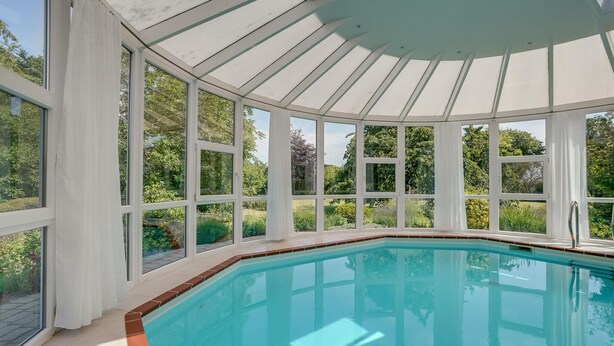 A sunlit indoor swimming pool with large windows and a white ceiling.