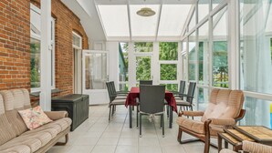 A sunroom with a brick wall, large windows, and a dining area with chairs and a table.