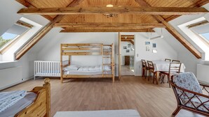 A cozy attic bedroom with a bunk bed, a dining table with chairs, and a view of the outside through skylights.