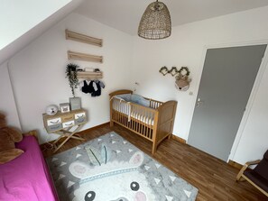 A cozy baby room with a crib, a dresser, a hanging plant, and a decorative headboard.