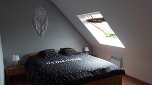 Une chambre avec un plafond en pente, un puits de lumière, un lit recouvert d’une courtepointe noire, deux lampes de chevet et un attrape-rêves accroché au mur.