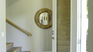 Un pasillo con una escalera curva, un espejo redondo en la pared y una puerta con panel texturizado.