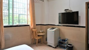 A hotel room with a bed, a desk, a chair, a television, an air conditioner, and a window with curtains. - Wenxin Hotel (Sihui)