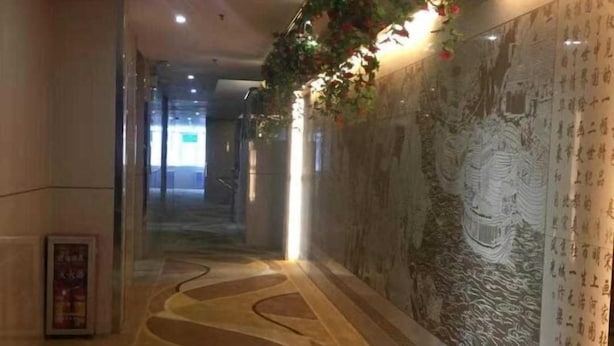 A hallway with a patterned floor, a wall with calligraphy, and a poster on the left. - Wenxin Hotel (Sihui)