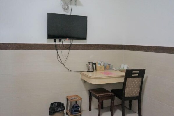 Una habitación pequeña con una televisión de pantalla plana montada en la pared, un escritorio con una silla y una mesita con un calentador.
