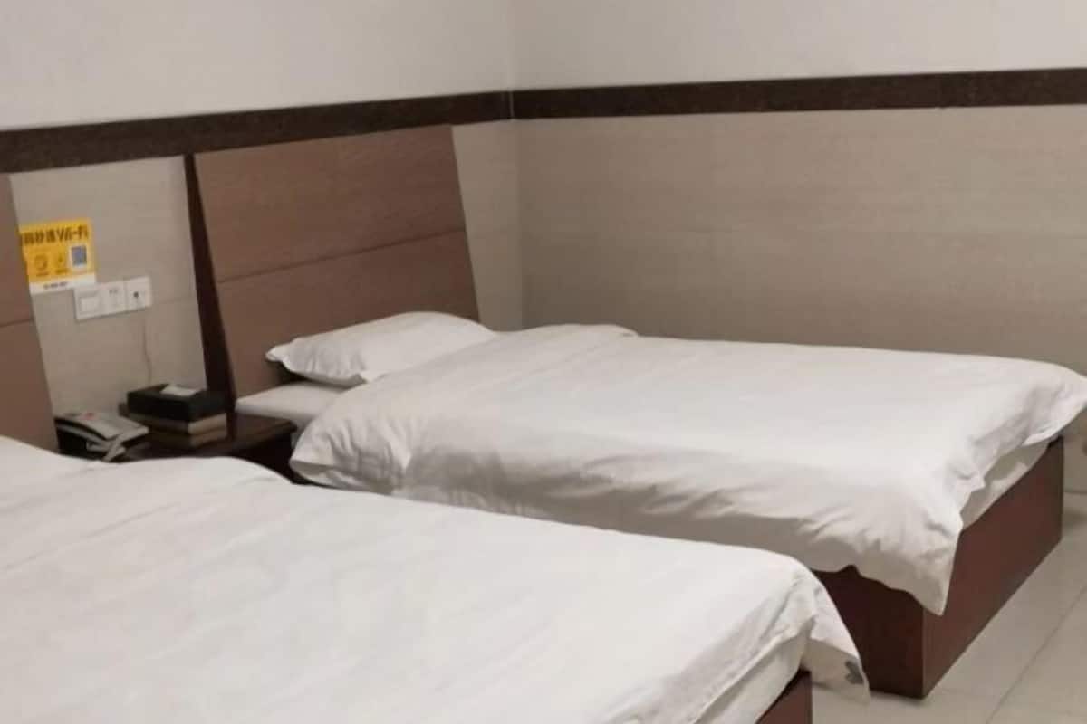 A hotel room with two single beds, a wooden headboard, a nightstand with a phone, and a wall-mounted light switch.