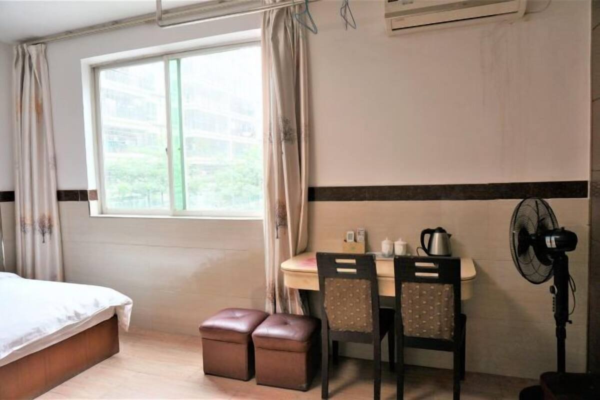 A room with a bed, a table with chairs, a fan, and a window with curtains.