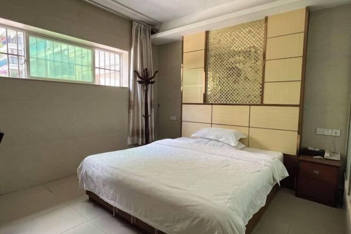 A bedroom with a bed, a window, a nightstand, and a decorative panel.