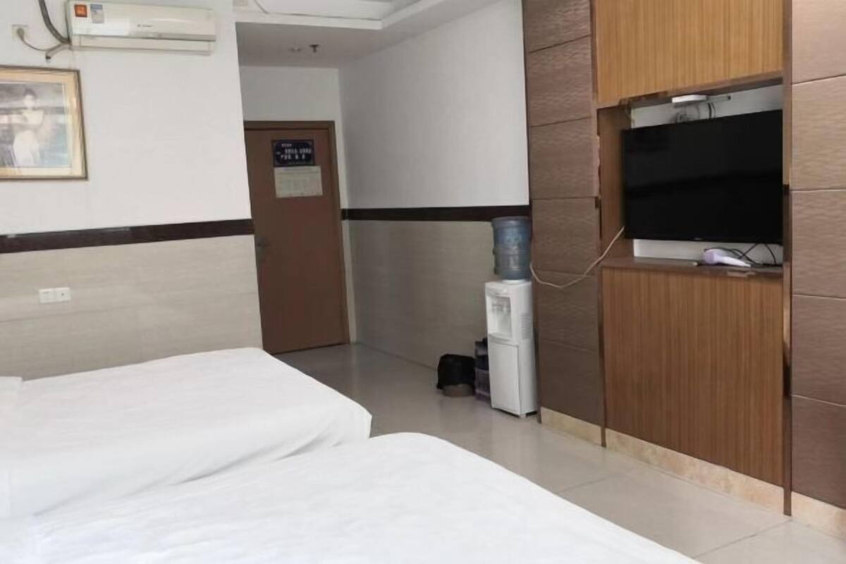 A hotel room with two beds, a water dispenser, a television, and a door with a sign.