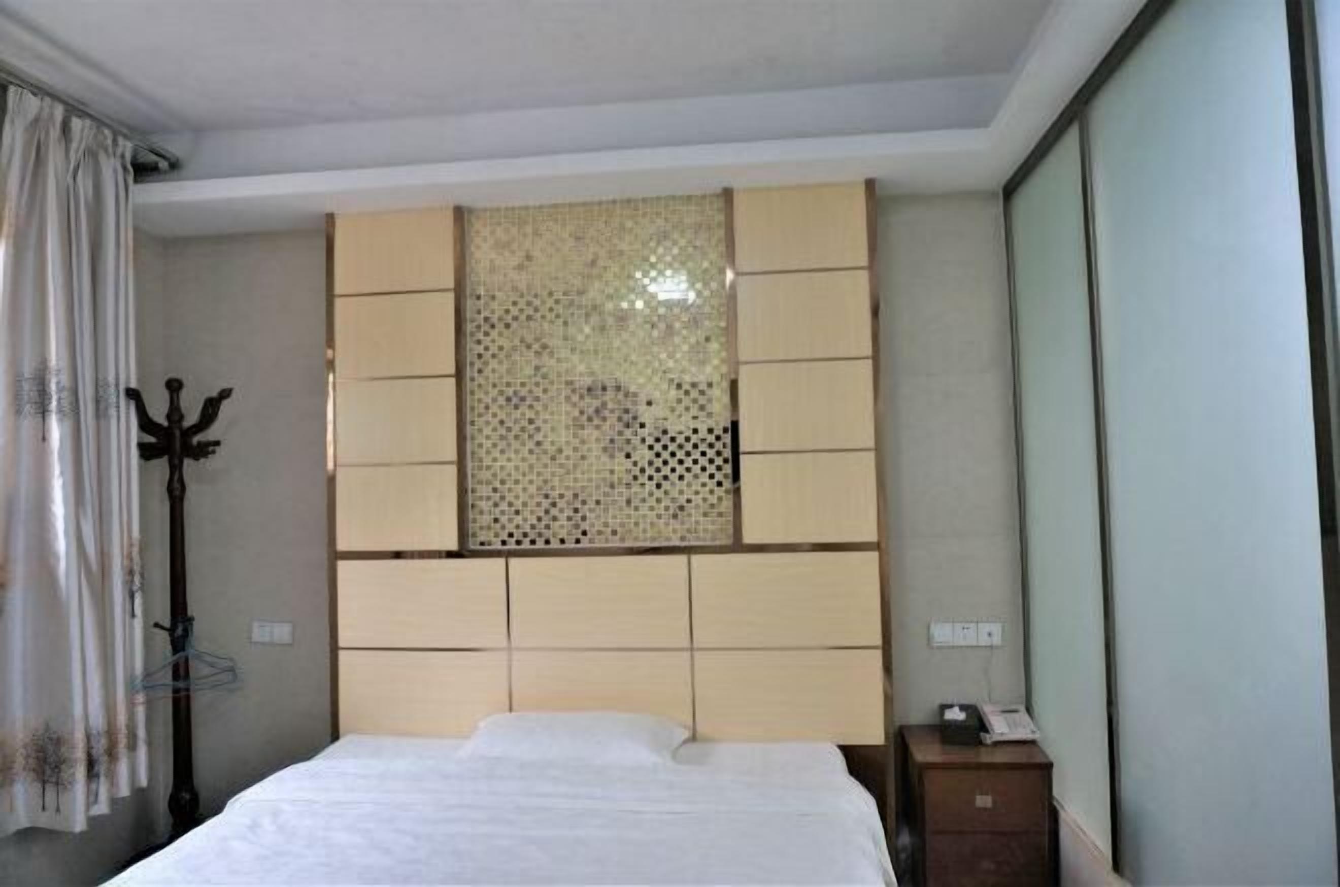 Een hotelkamer met een bed, een tv aan de muur, een kapstok en een raam met gordijnen.