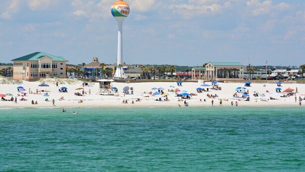 Une plage avec un château d’eau, des parasols et un bâtiment doté d’un toit végétalisé.