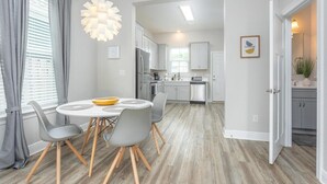 Une cuisine moderne avec des meubles blancs, un réfrigérateur en acier inoxydable et un coin repas comprenant une table ronde et des chaises.