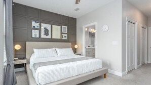 Une chambre à coucher avec un grand lit, des tables de chevet, une commode, un meuble à tiroirs, un miroir et une porte.