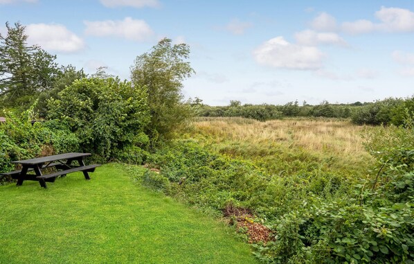 A picnic area with a wooden table and benches surrounded by lush greenery and a field.