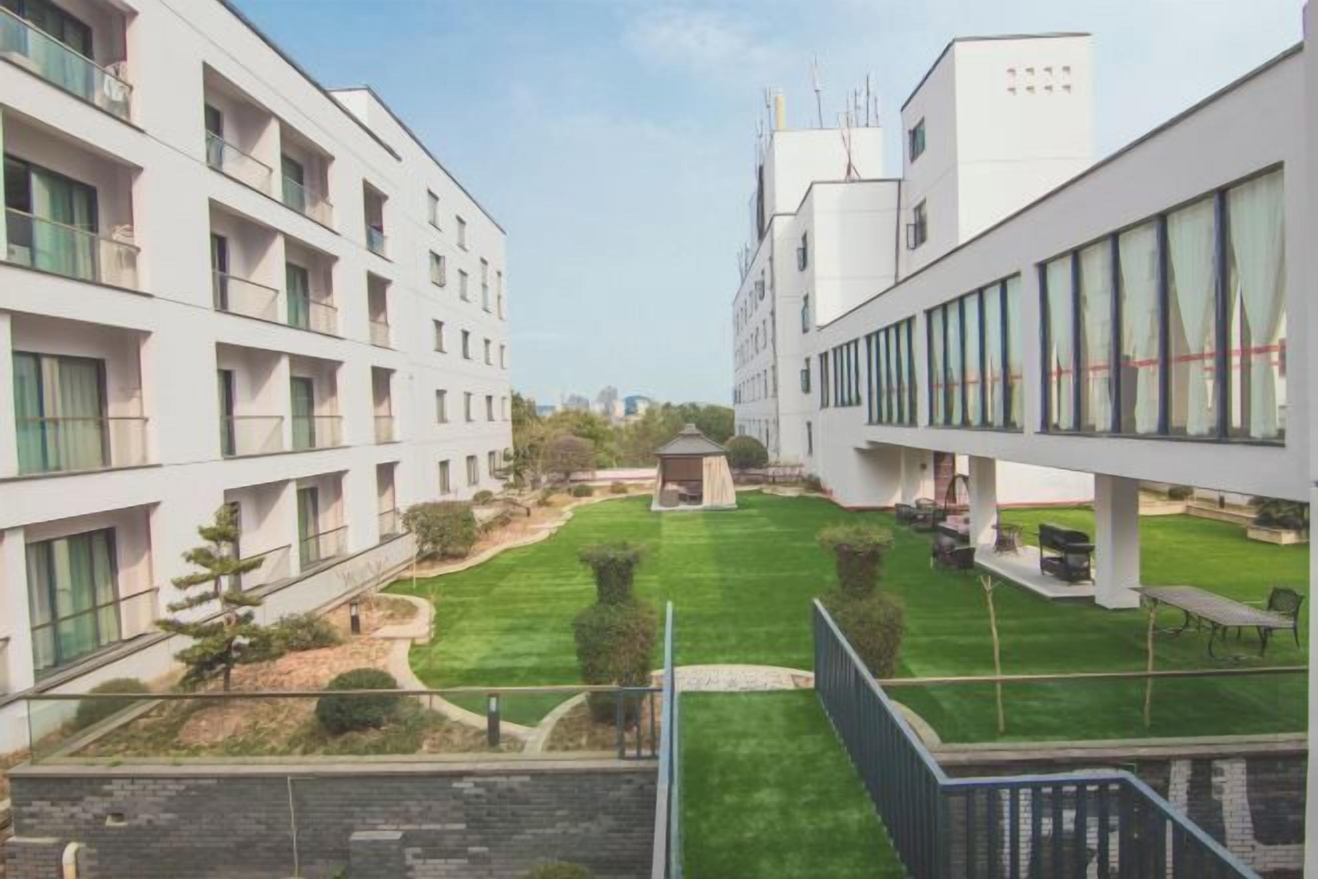 A modern building with multiple floors, a central courtyard with grass, and a small gazebo.