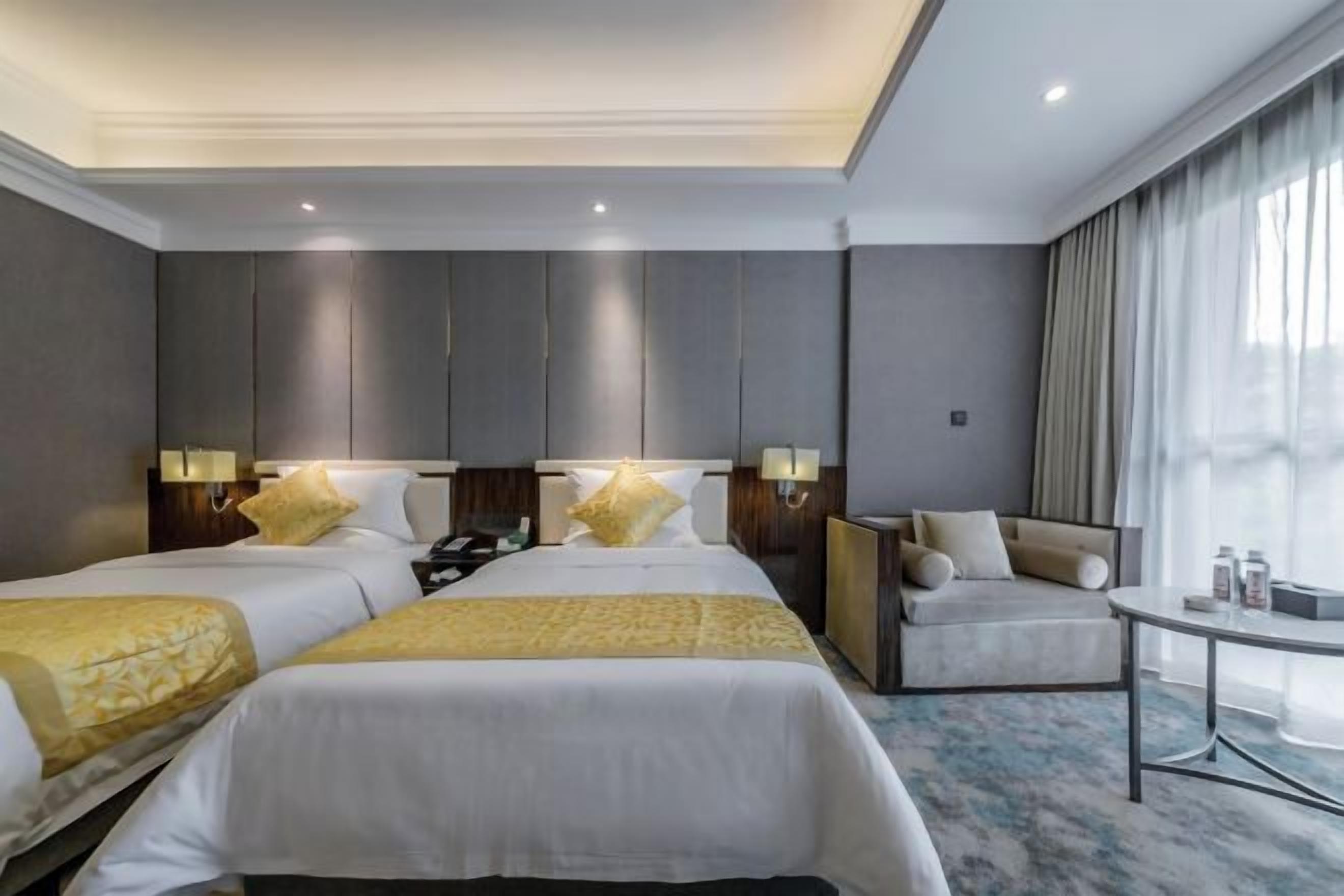 A hotel room with two beds, a sofa, a small table, and a view of the outdoors.