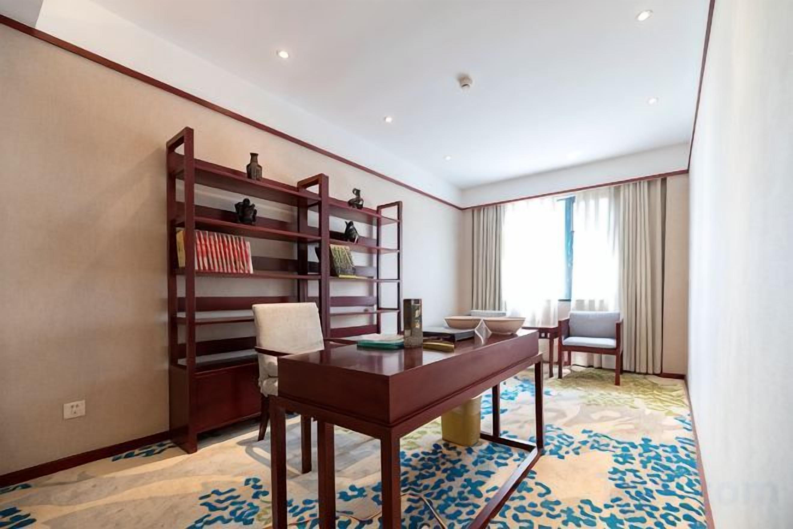 Habitació d'hotel amb una biblioteca de fusta, una taula de menjador amb cadires i un gran finestral amb cortines.
