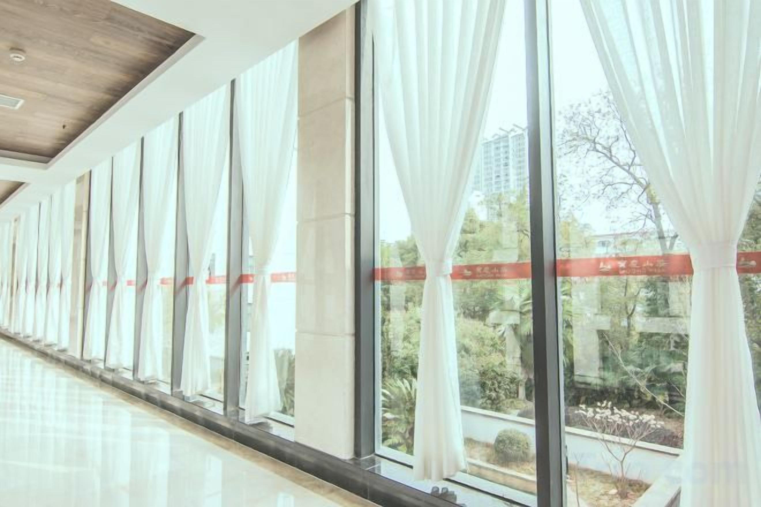 A corridor with large windows, white curtains, and a polished floor.