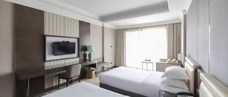 A hotel room with two beds, a desk, a TV, and a window with curtains.